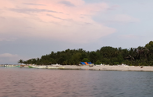 A tropical island at sunset with fishing boats moored on the sandy beach.