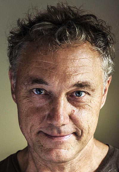 A man with curly greyish hair wearing a brown t-shirt