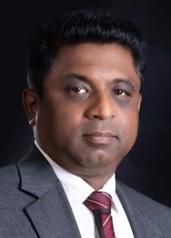 Portrait of a man in a suit and tie against a dark background. He looks directly at the camera with a calm, neutral expression.