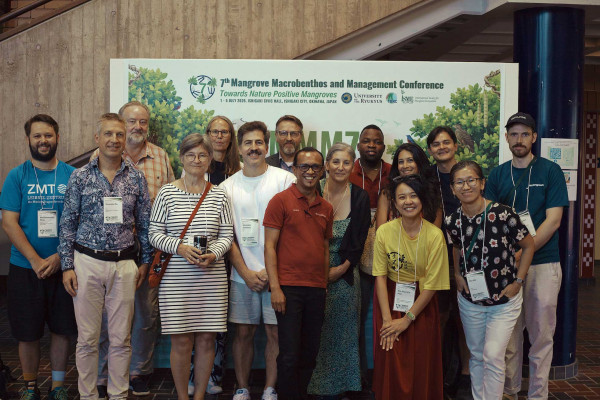 Gruppenfoto von Teilnehmenden der 7. Mangrove Macrobenthos and Management Conference vor einer Konferenzwand mit dem Motto „Towards Nature Positive Mangroves“. Die Gruppe blickt lächelnd in die Kamera und steht dicht beieinander. 
