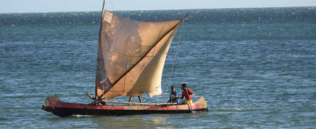 Small fishing boat with a square sail and two fishers in the sea off Madagascar