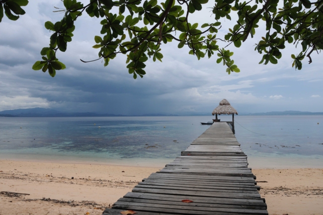 A long wooden pier leads to a small thatched hut in the sea in Manado, Indonesia